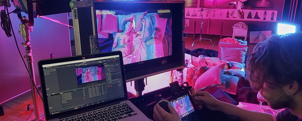 Zdjęcie przedstawiające fragment pracowni w czasie zajęć z widocznymi fragmentami ekranów w czasie postprodukcji. Zdacie zachowane w kolorystyce różowo fioletowej.j