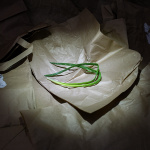 Fotografia kolorowa w pionie przedstawiająca pogniecione torby papierowe. Na jednej z toreb w centrum kadru widać zielony szczypior